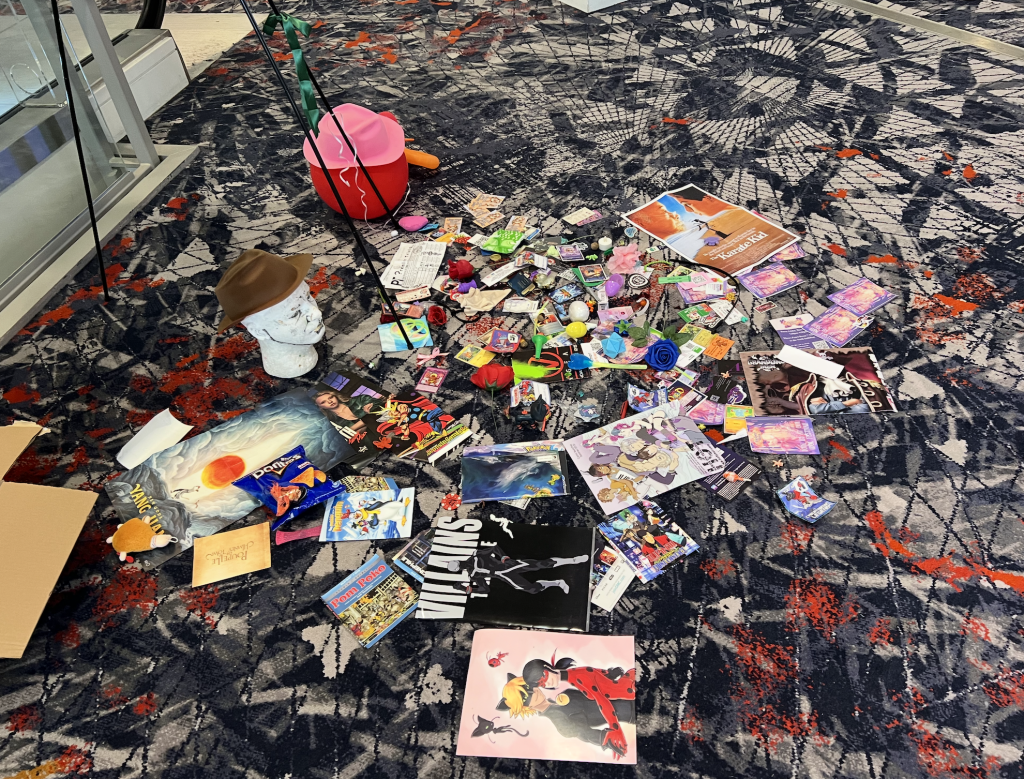 The 2026 collection of gifts including Pokemon cards, a wig head in a brown cowboy hat, fan art, movie posters, and roses. 